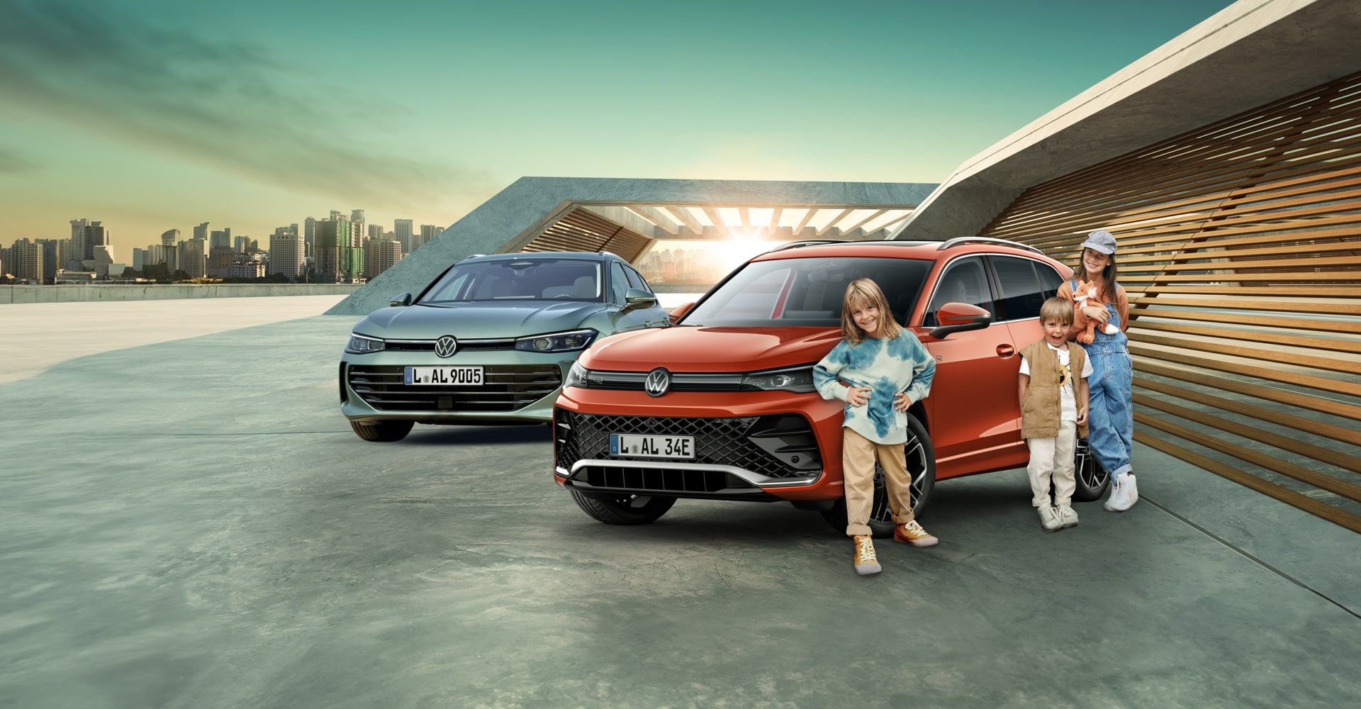 3 Kinder stehen vor einem Persimmon Red Metallic VW Tiguan. Links davon befindet sich ein neuer Passat in Maripositgrün Metallic. Im Hintergrund erkennt man eine Skyline und ein modernes Gebäude.